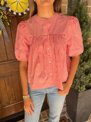 Up close photo of a woman standing in front of a door wearing an orange and white striped blouse
