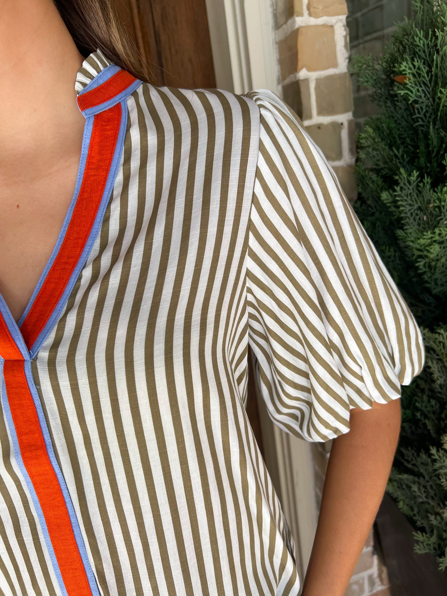 Another up close photo of a cream and khaki striped short sleeve blouse with an orange and blue stripe around the collar and down the front 