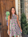 Woman in a pink and green patterned dress standing in front of a wooden door.