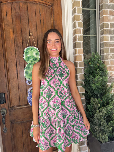 Woman in a pink and green patterned dress standing in front of a wooden door.