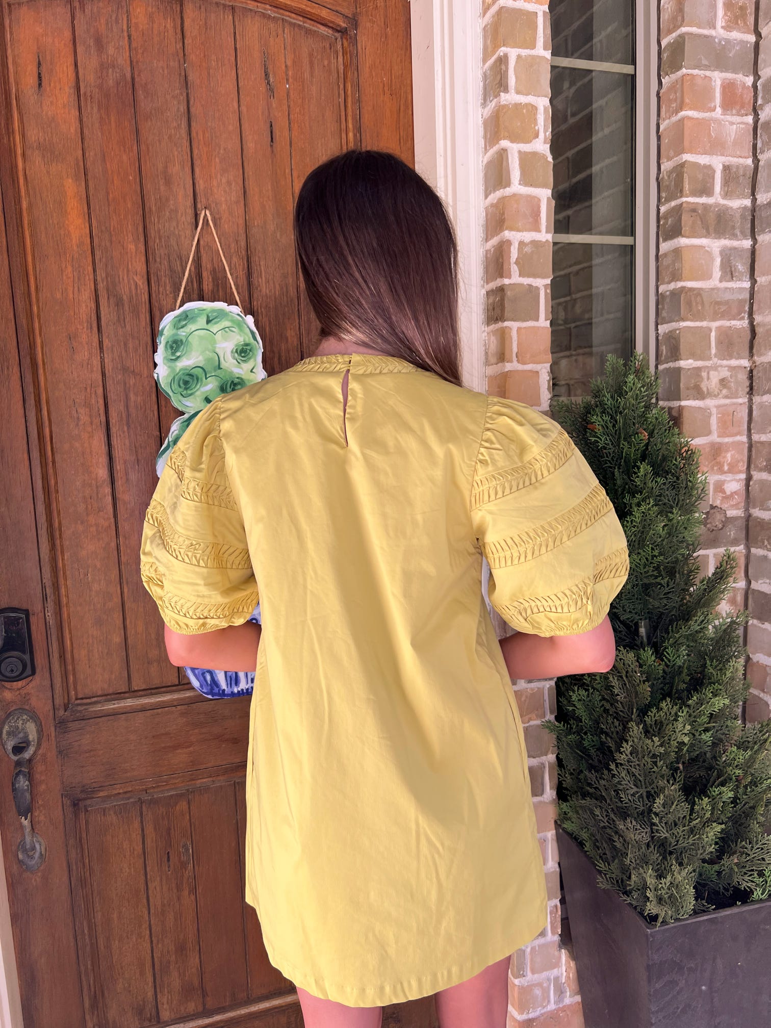 Photo of the back of a person wearing a chartruse colored dress standing in front of a wooden door.