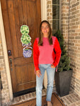 Woman standing in front of a door wearing a pink long sleeve sweater with orange sleeves