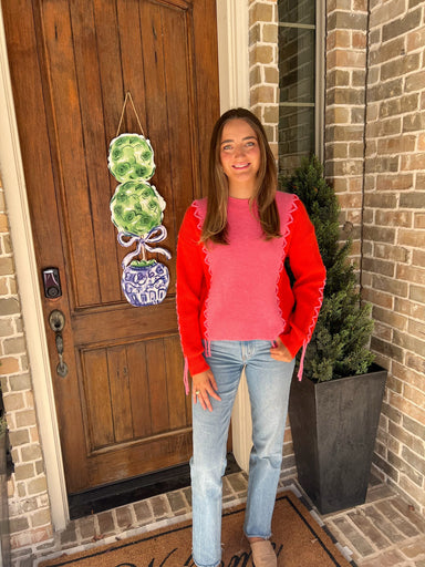 Woman standing in front of a door wearing a pink long sleeve sweater with orange sleeves