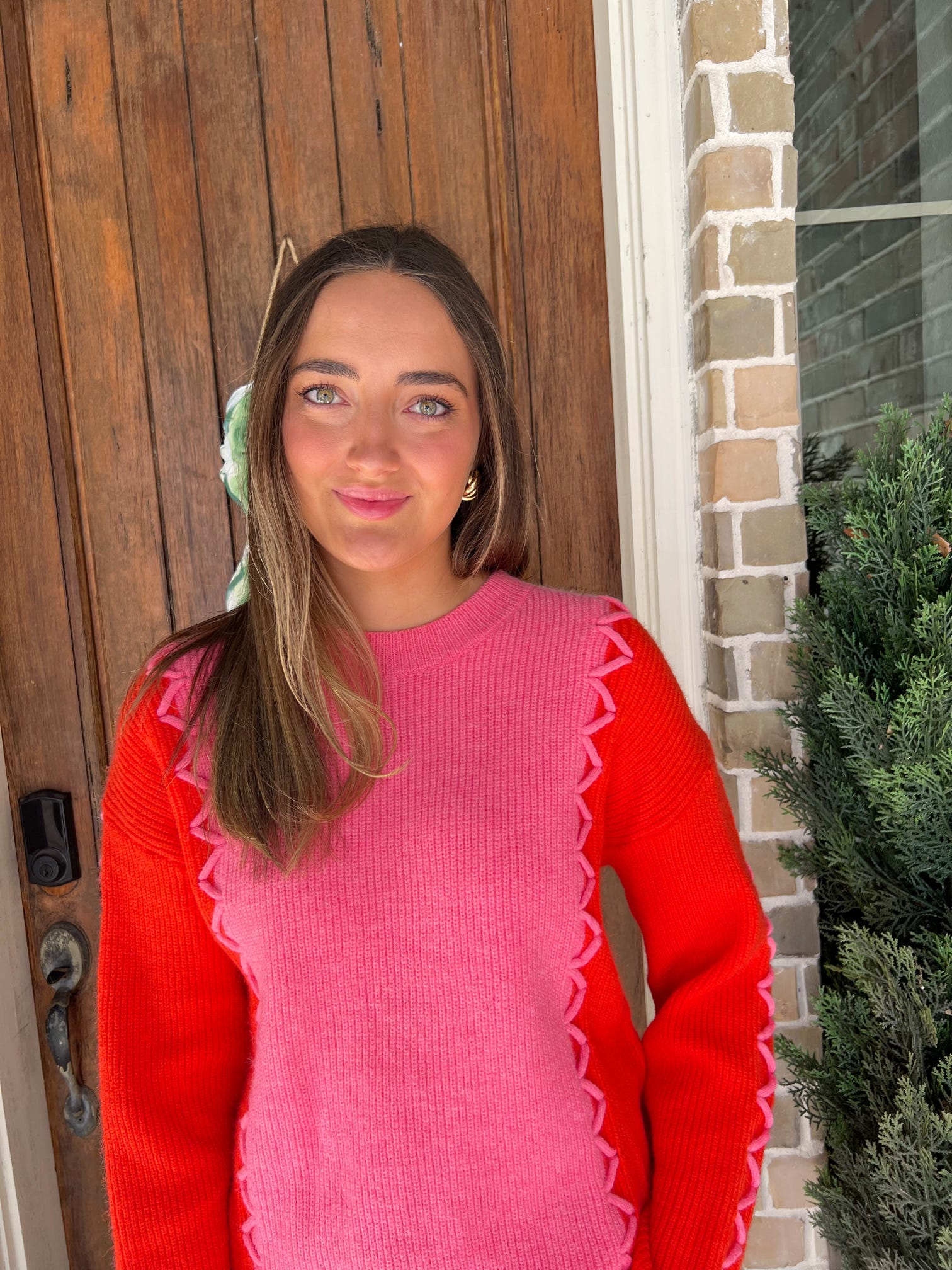 Close up photo of a woman standing in front of a door wearing a pink long sleeve sweater with orange sleeves