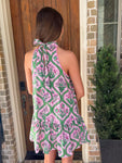 Photo of the back of the dress of a woman wearing a pink and green patterned dress standing in front of a brick house.