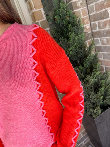 Up close photo of a pink long sleeve sweater with orange sleeves