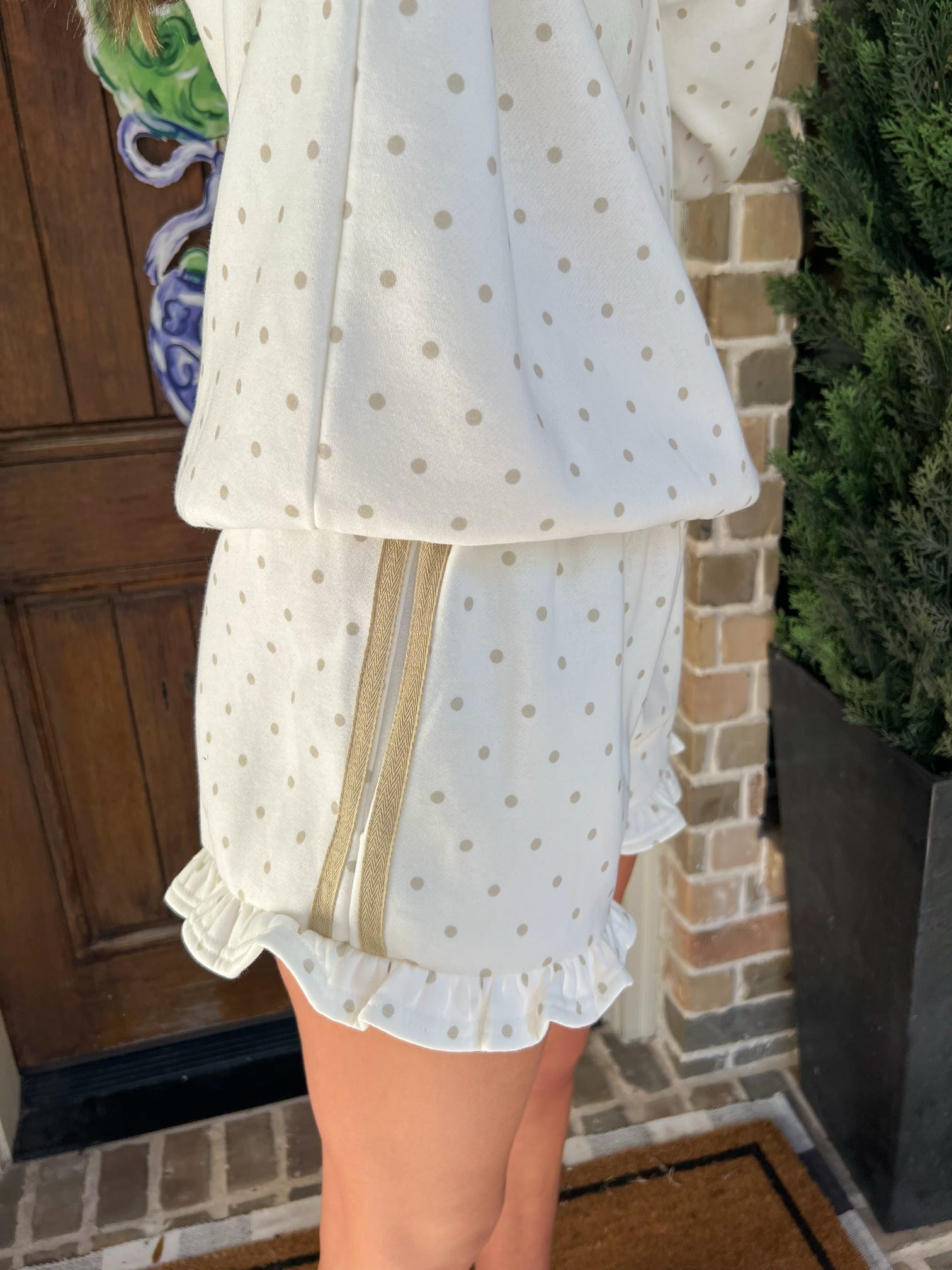 Up close photo of the polka dot shorts showing the cream color with khaki dots and two stripes running down the side of the shorts with a ruffle on the bottom