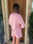 Person wearing a pink and white striped outfit standing in front of a wooden door.