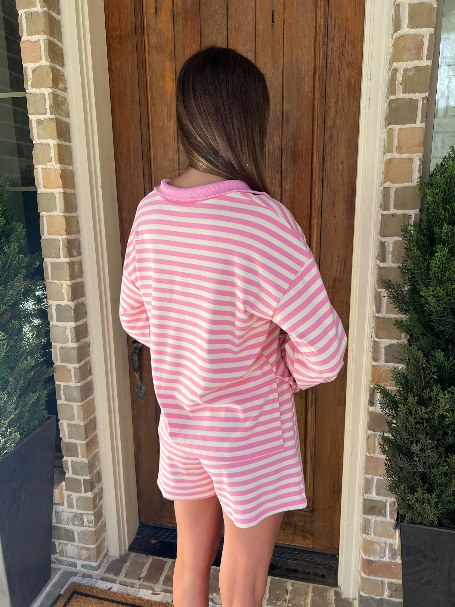 Person wearing a pink and white striped outfit standing in front of a wooden door.