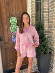 Woman in pink and white striped shorts set standing outside a house.