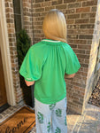 Photo of the back of a woman wearing a  green blouse standing in front of a brick wall.