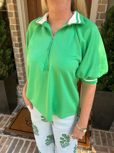 Person wearing a green quarter-zip shirt with white trim in front of a brick wall.