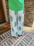 Up close photo of the back of a woman wearing white pants with green floral patterns in front of a brick wall.