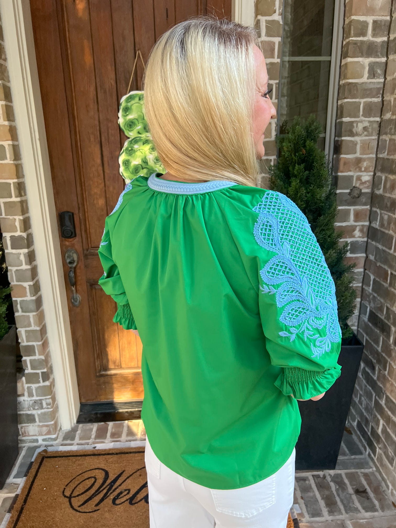 Photo of the back of a woman wearing a green blouse with lace sleeves standing outside a house.