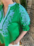 Up close photo of the bubble sleeve of a green blouse with white embroidery on a person standing outdoors.