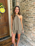 Woman in a polka dot romper standing in front of a brick wall and wooden door.