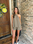 Woman in a polka dot romper standing in front of a brick wall and wooden door with a wreath.