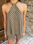 Person wearing a polka dot romper in front of a brick wall.