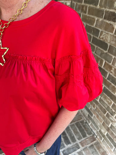 Person wearing a red blouse with puffed sleeves against a brick wall.