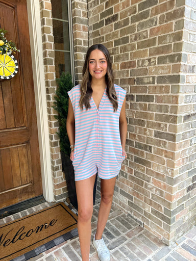 Woman in a light pink/ baby blue striped sleeveless romper standing outside a house with a 'Welcome' mat.