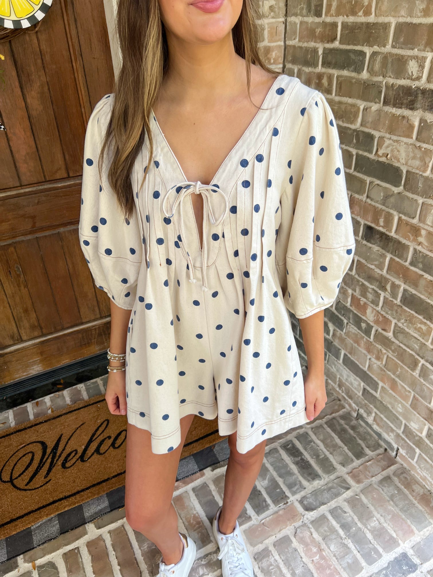 Woman wearing a polka dot dress standing in front of a brick wall.