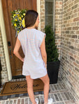 Woman showing the back of a light pink & baby blue striped sleeveless romper standing in front of a brick wall.