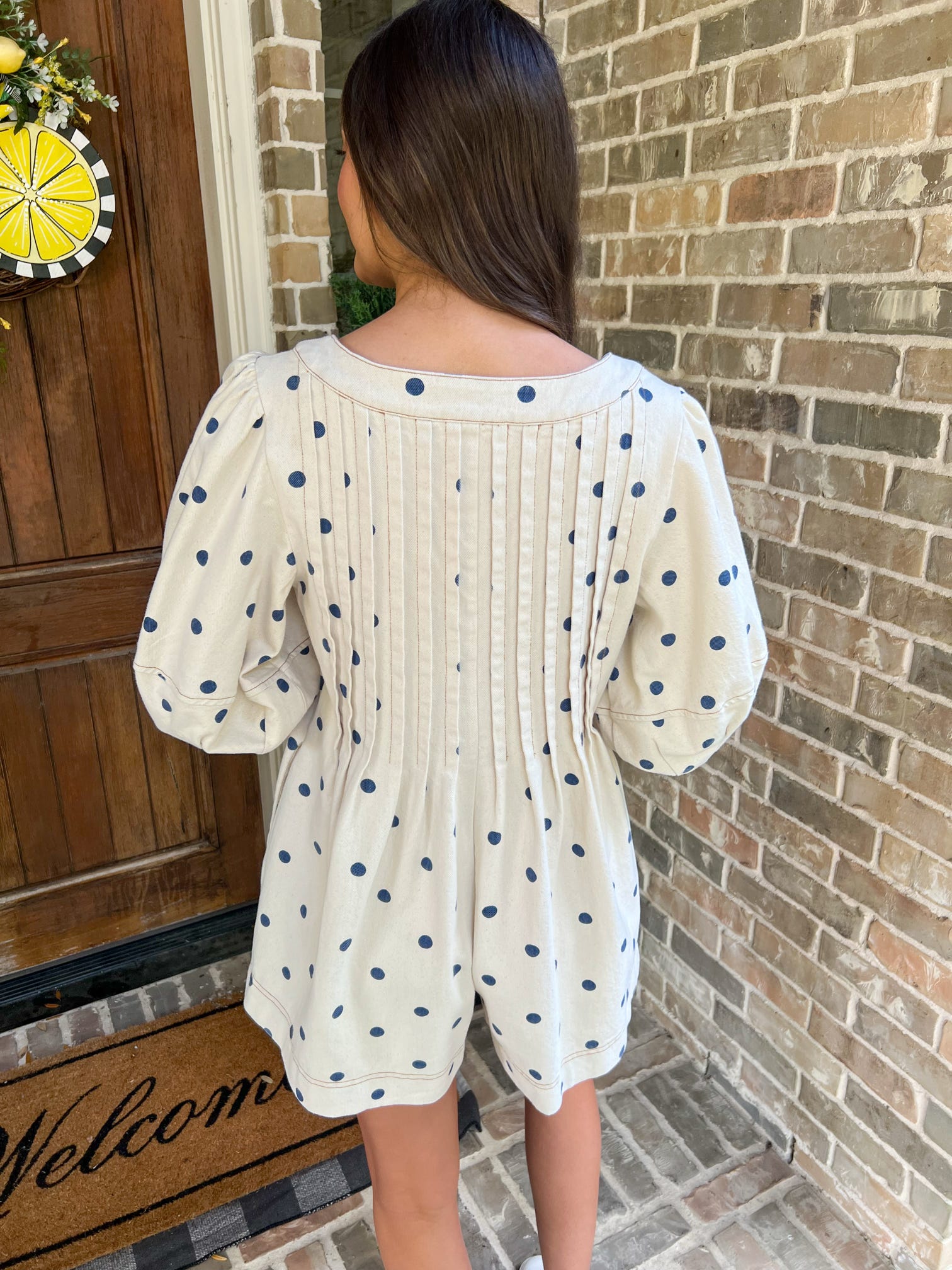 Woman wearing a polka dot dress standing in front of a brick wall.