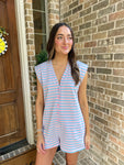 Woman wearing a light pink & baby blue striped sleeveless romper standing in front of a brick wall.