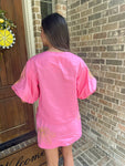 Person wearing a pink outfit standing in front of a brick wall.