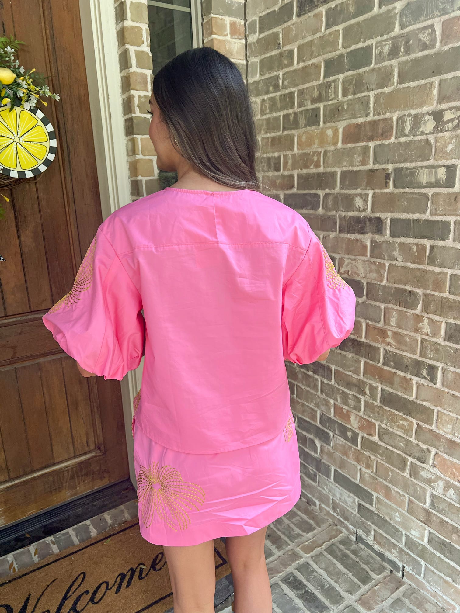 Person wearing a pink outfit standing in front of a brick wall.