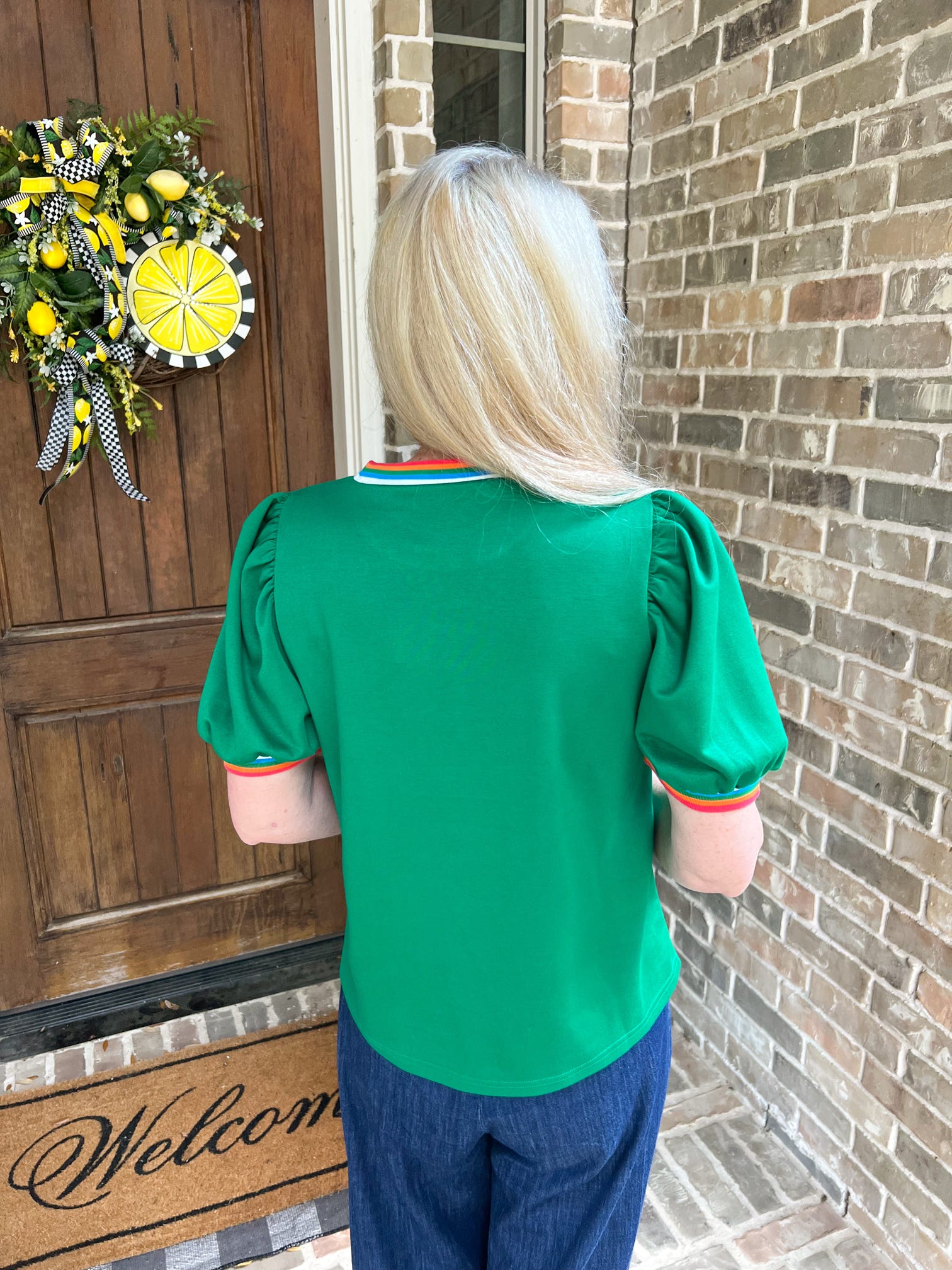 Person wearing a green shirt and blue pants standing in front of a door with a wreath.