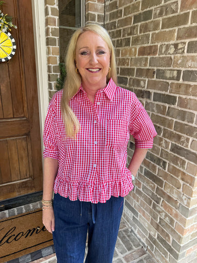 Woman wearing a red & white checkered shirt standing in front of a brick wall.
