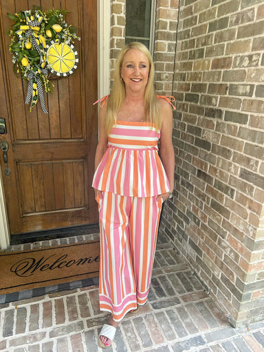 Woman in a striped outfit standing on a porch with a wreath and 'Welcome' mat.
