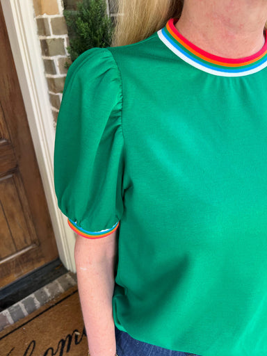 Green blouse with rainbow trim worn by a person, standing in front of a door.