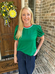 Woman in a green shirt standing in front of a door with a wreath, wearing a watch.