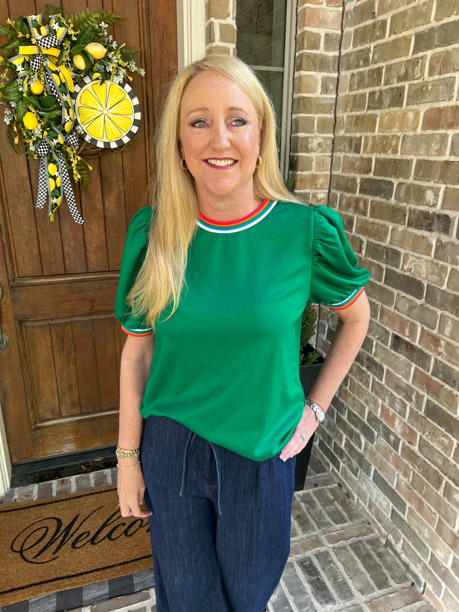 Woman in a green shirt standing in front of a door with a wreath, wearing a watch.
