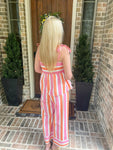 Person wearing a pink and orange striped outfit standing outside a house.
