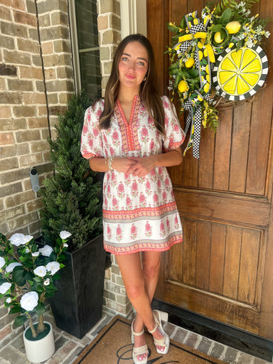 Woman standing in front of a door with decorative wreath and plants.