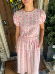 Person wearing a pink floral matching top & skirt set standing outside a house.