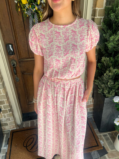Person wearing a pink floral matching top & skirt set standing outside a house.