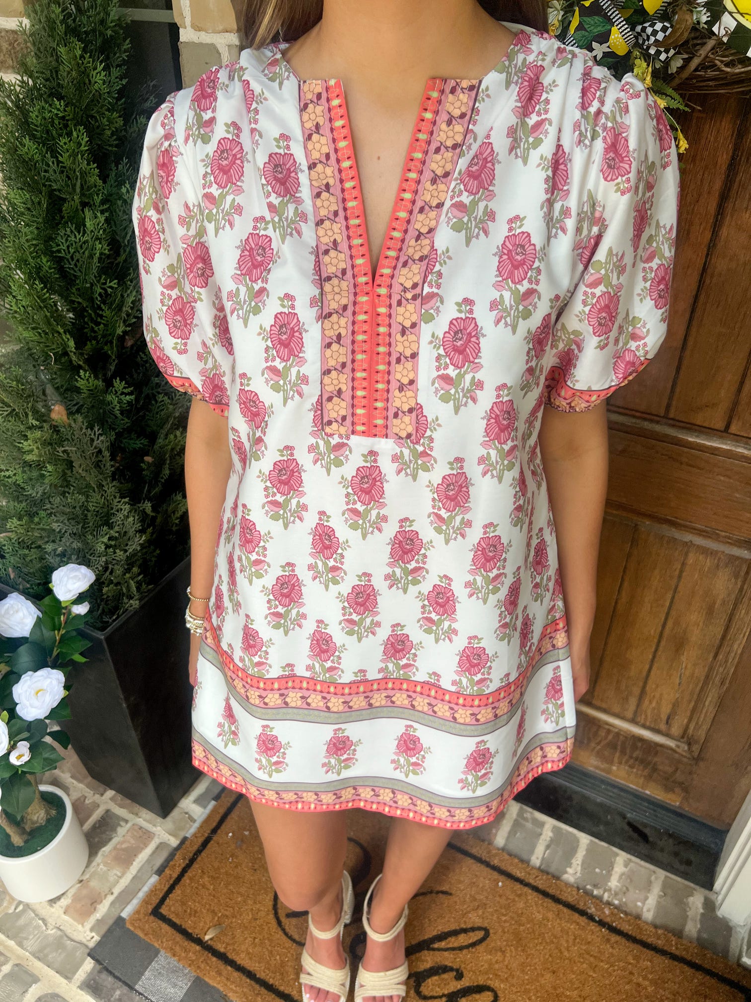 Person wearing a floral dress standing in front of a wooden door.