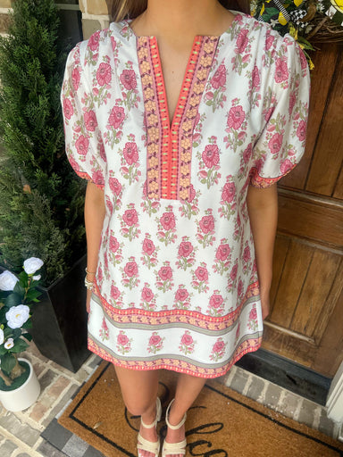 Person wearing a floral dress standing in front of a wooden door.