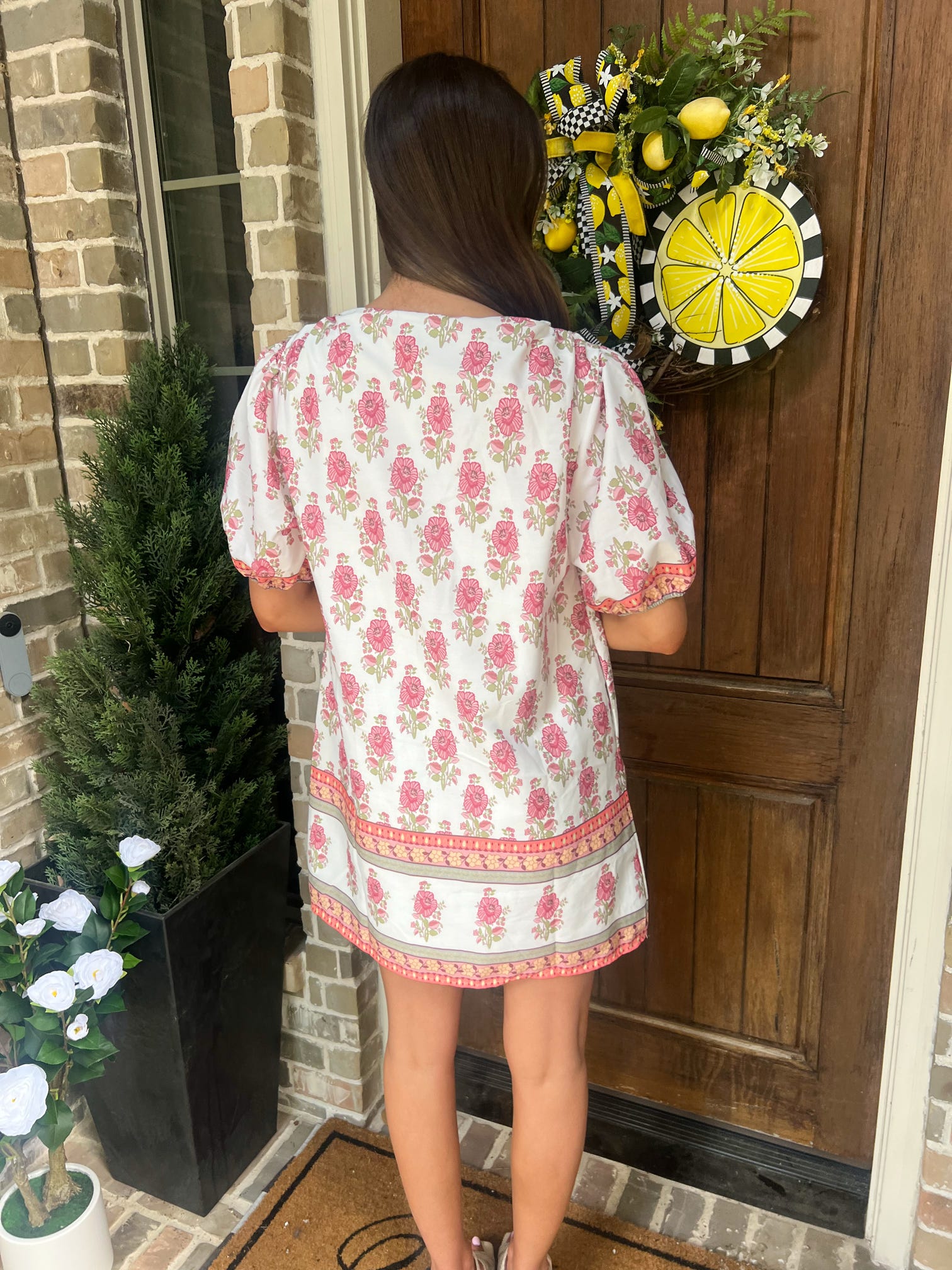 Person wearing a floral dress standing in front of a door with a decorative wreath.