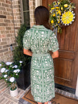 Woman showing the back of a green floral dress standing in front of a door with a decorative wreath.