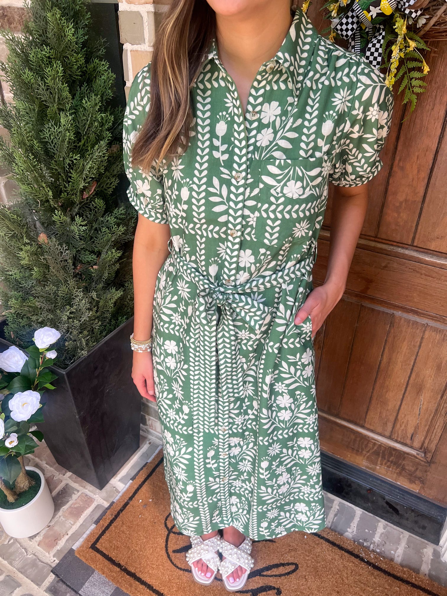 Person wearing a green and cream patterned dress standing in front of a wooden door.