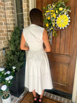 Woman in a white with small black polka dots dress standing in front of a wooden door with a decorative wreath.
