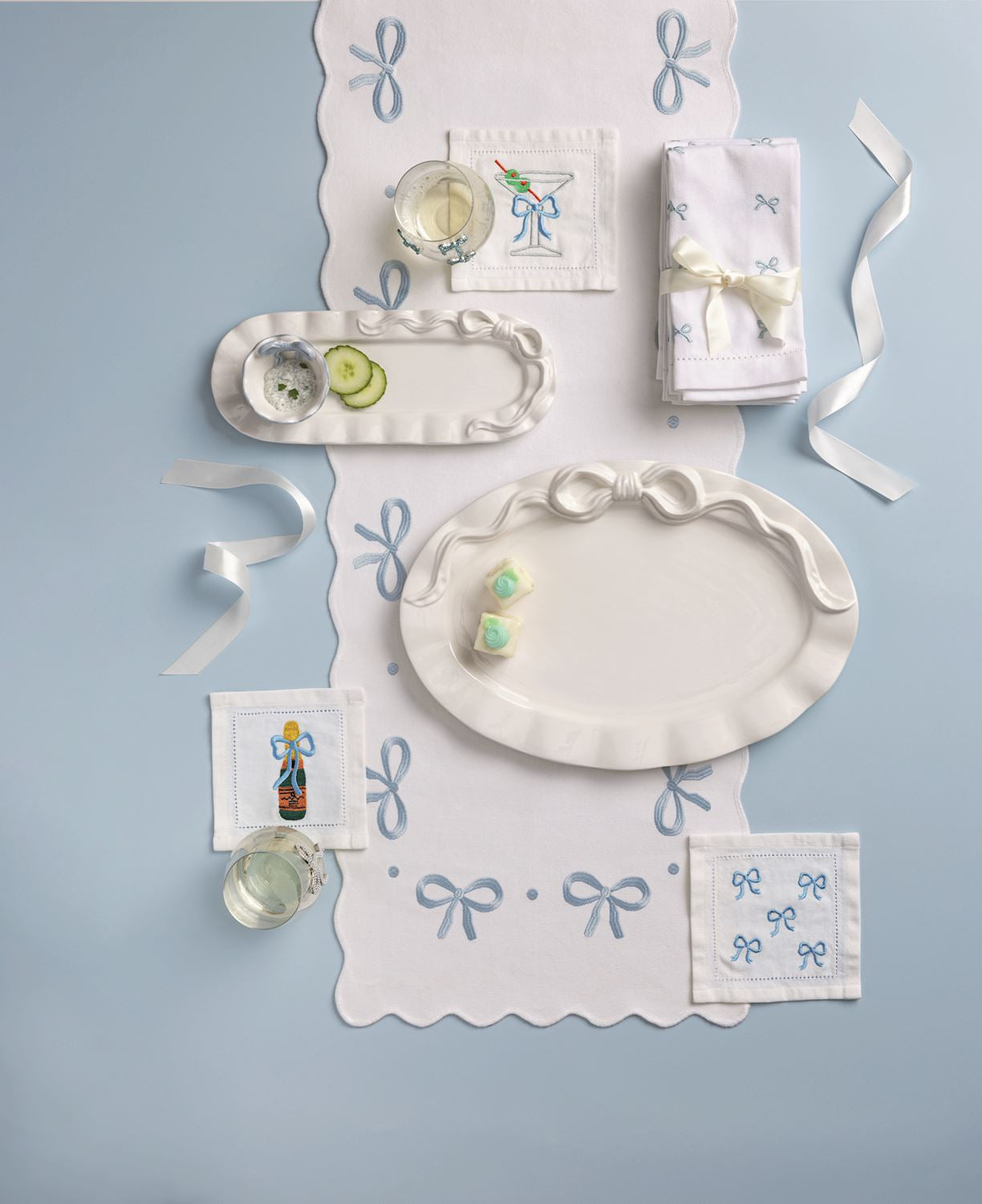 Decorative table setting with white plates, napkins, and small items on a light blue background. All items have bows on them.