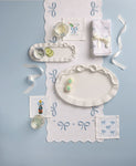 Decorative table setting with white plates, napkins, and small items on a light blue background. All items have bows on them.