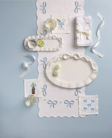 Decorative table setting with white plates, napkins, and small items on a light blue background. All items have bows on them.