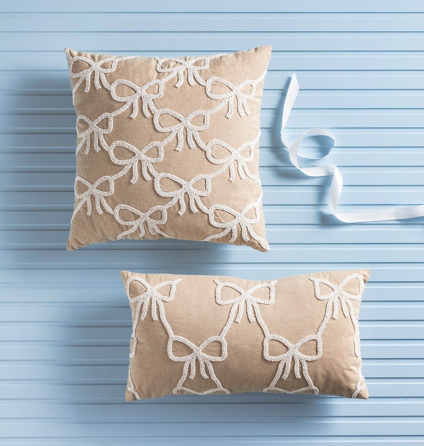 Two beige pillows with white bow patterns on a light blue wooden background